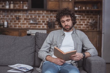 Junger Mann liest Buch auf der Couch.